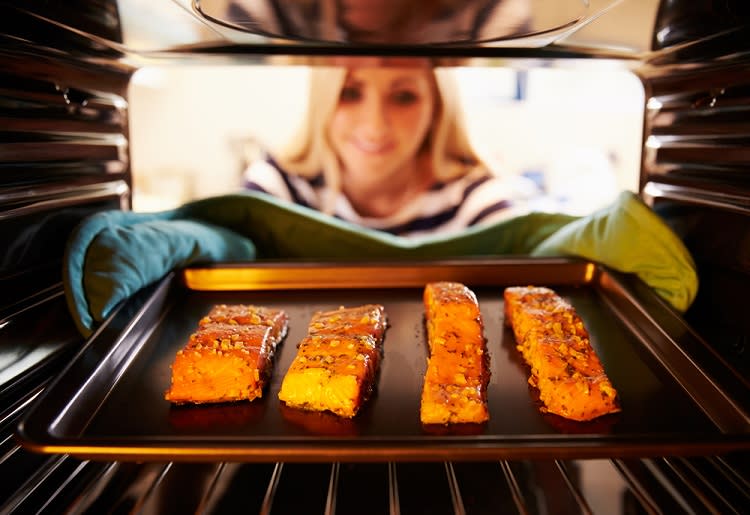 10 Fat-Burning, High-Protein Meals Pescatarians Love Woman removing tray of fish fillets from oven